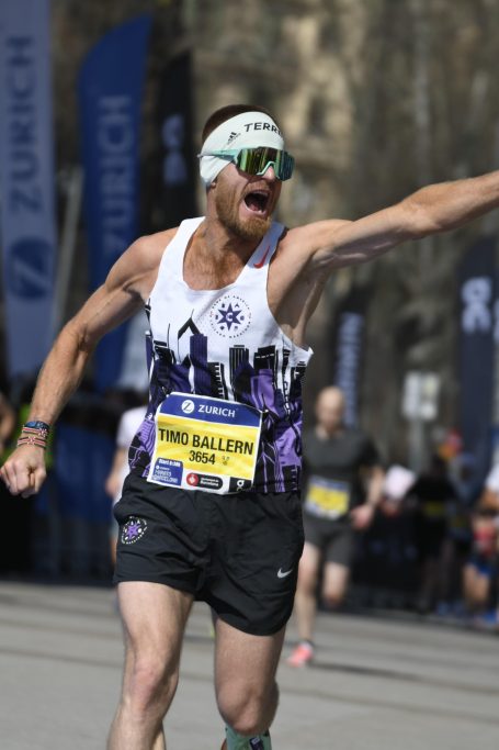 Läufer in Sportbekleidung mit erhobenen Armen, jubelt beim Zieleinlauf.